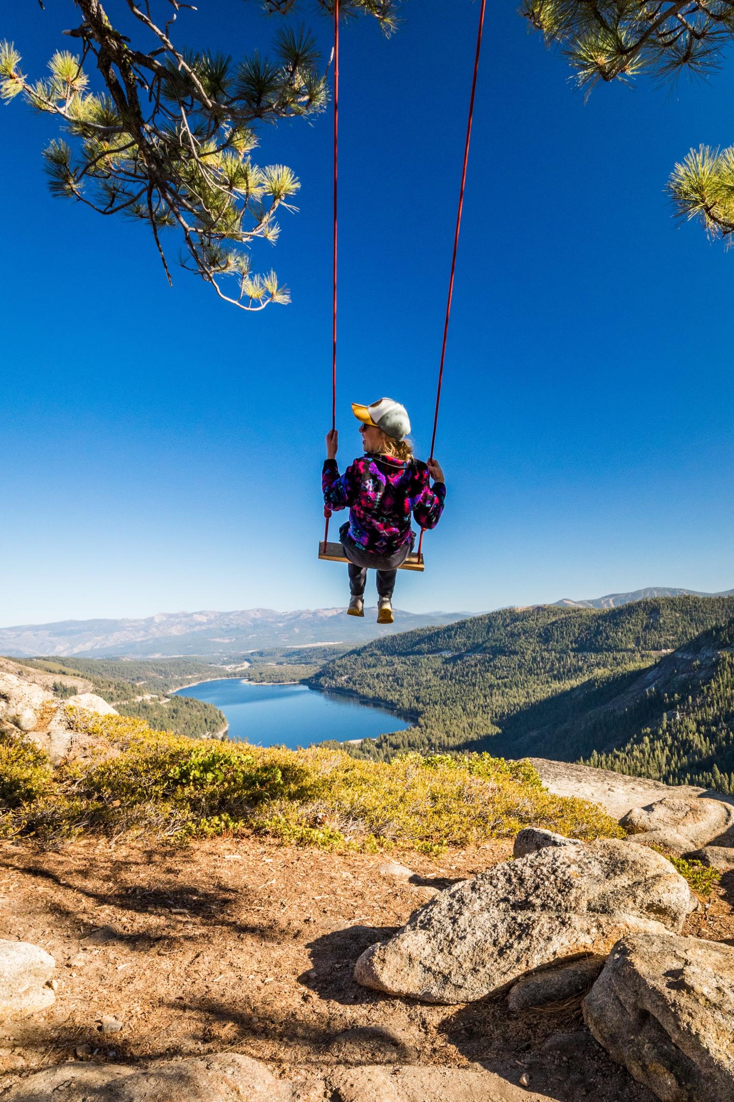Person in colorful outfit swinging over scenic mountain and lake view.