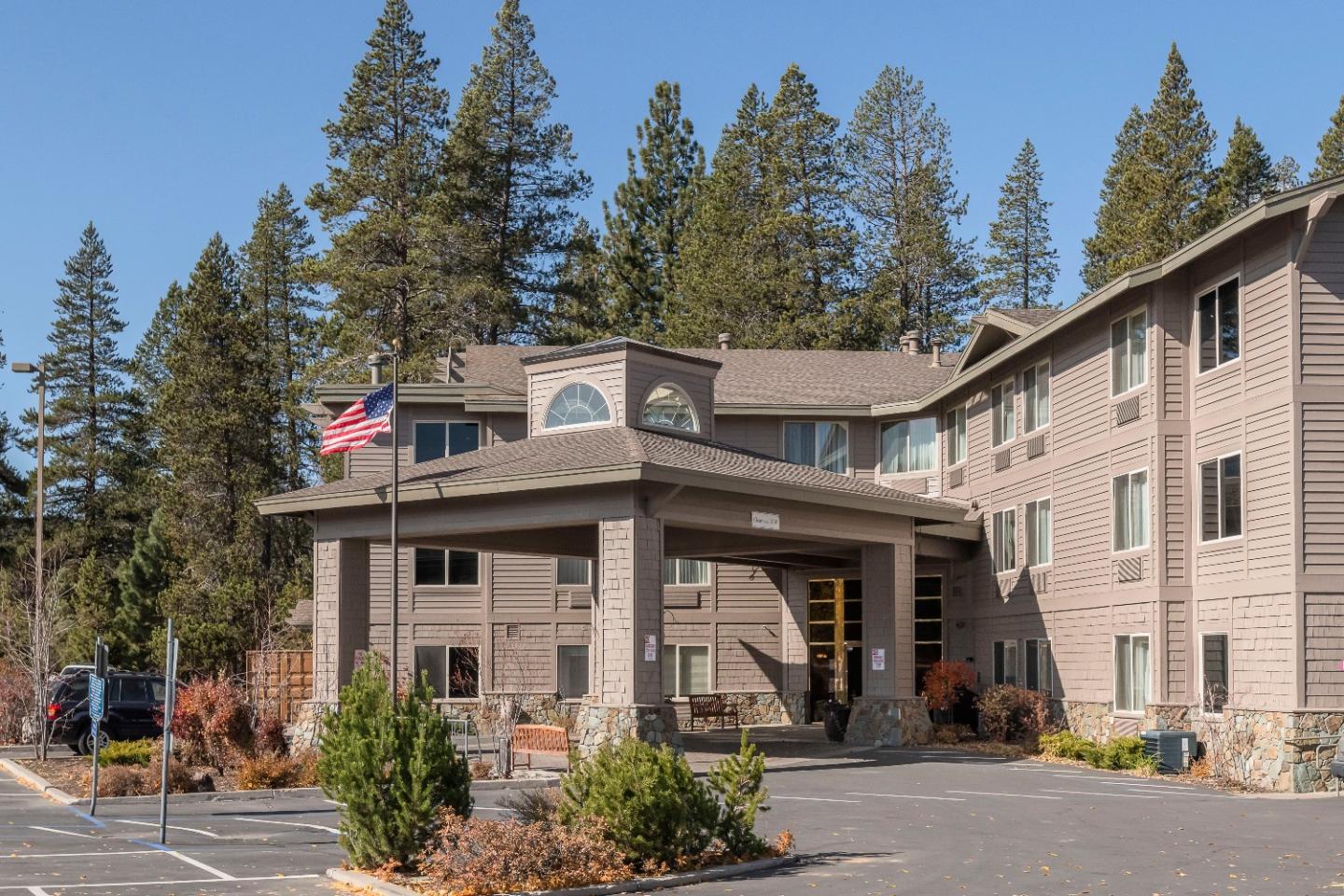Three-story rustic hotel with American flag, surrounded by tall pine trees.