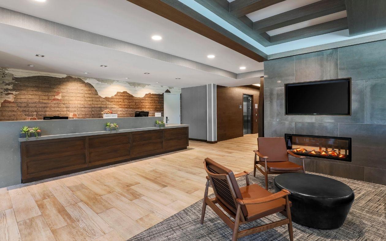 Modern lobby with wooden flooring, reception desk, chairs, fireplace, and wall-mounted TV.