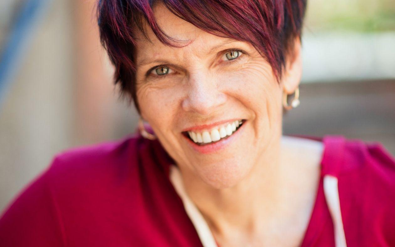 Smiling person with short dark red hair wearing a red top.