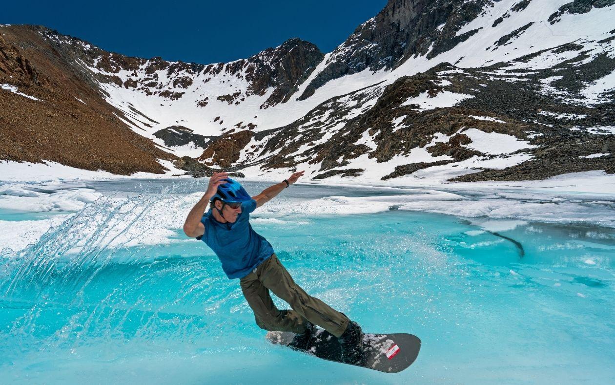 Snowboarder gliding across icy mountain terrain under clear blue sky.