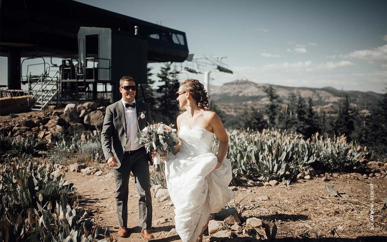 Bride and groom walking outside on rocky terrain, mountain backdrop.