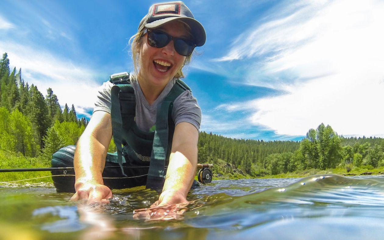 Person smiling while fishing in a river under a bright blue sky.