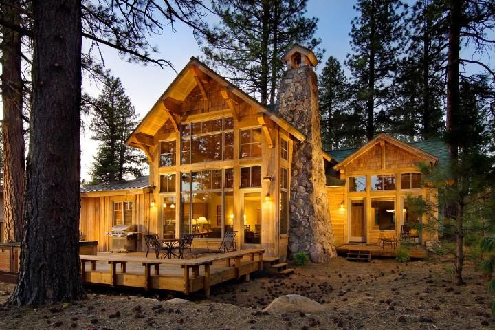 Cozy log cabin with large windows, surrounded by tall trees at dusk.