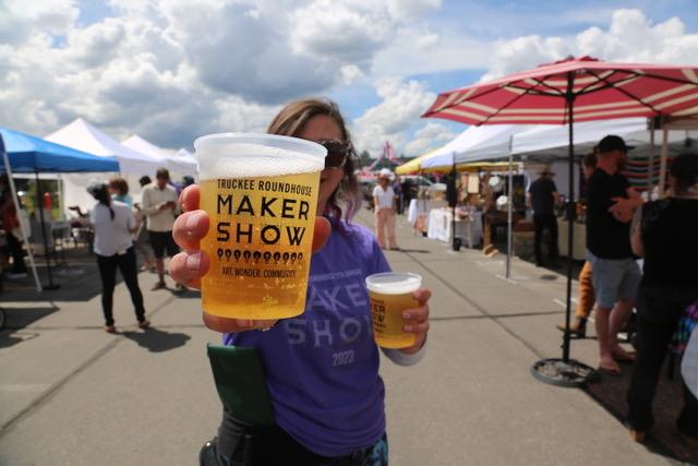 Person holding a cup of beer at an outdoor market under cloudy skies. Truckee Roundhouse Maker Show in Truckee, California