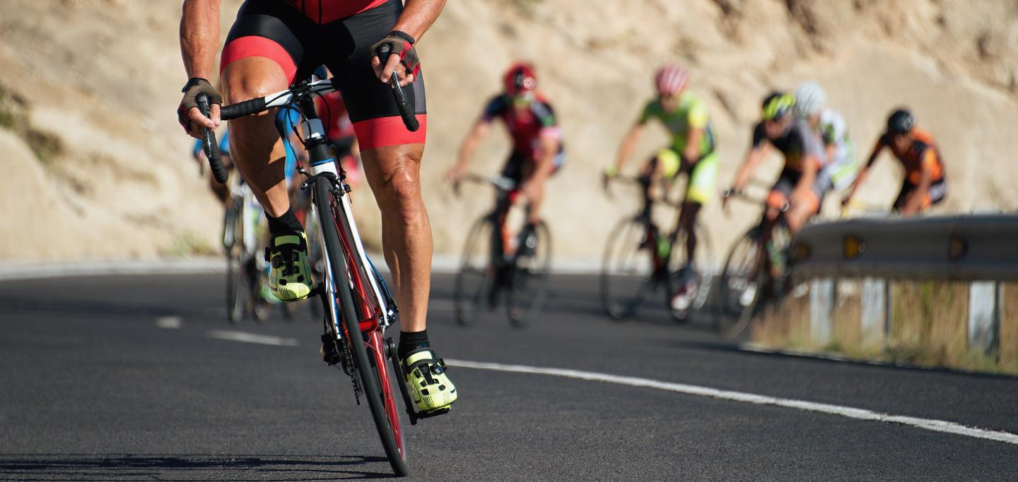 Cyclists race on a winding road, desert landscape in the background.