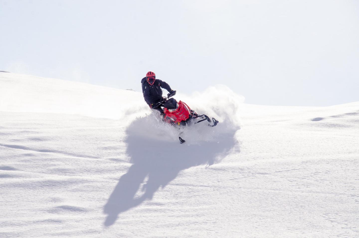 Snowmobiler riding fast on a snowy slope under a clear sky.