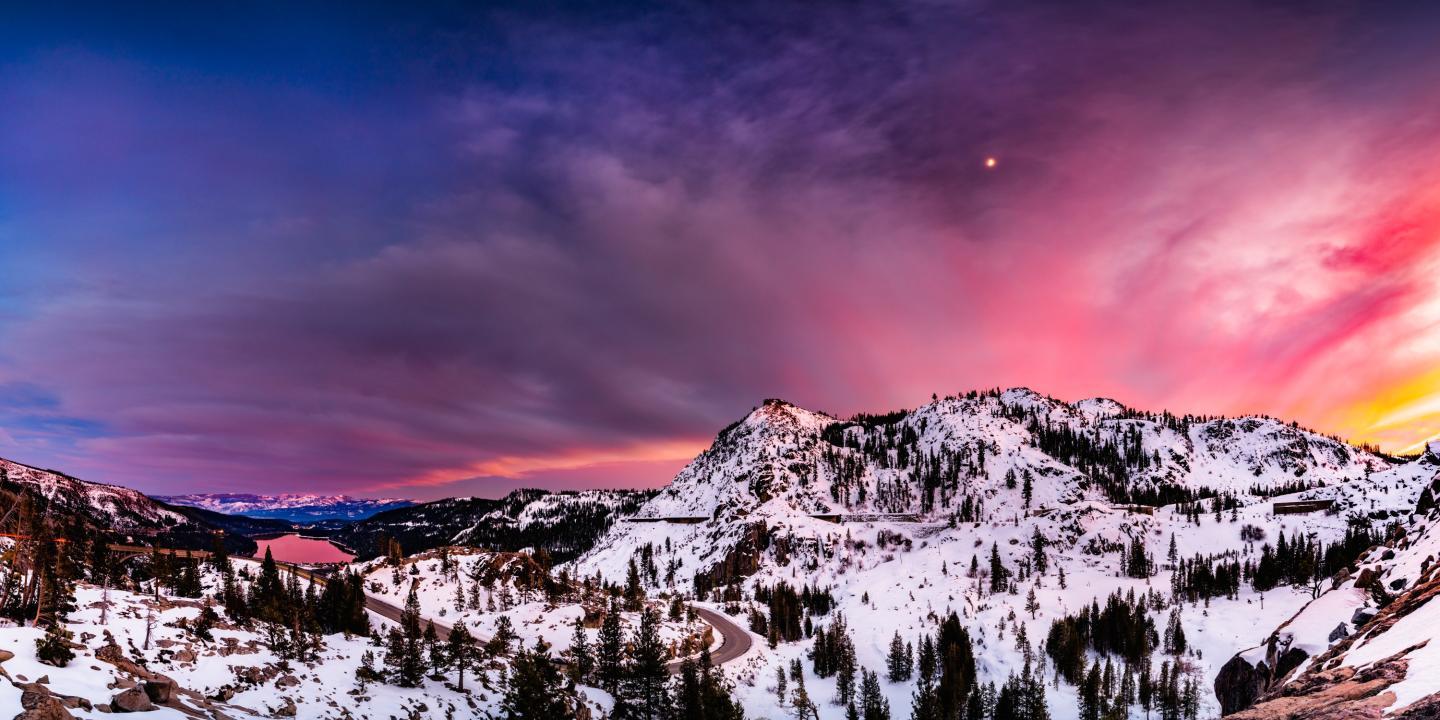 Snowy mountain landscape at sunset, with pink and purple sky.