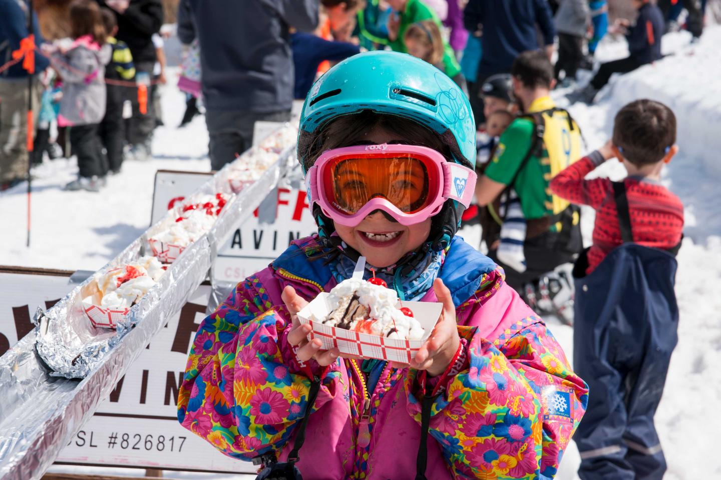 Child in colorful winter gear holding a dessert on a snowy day.