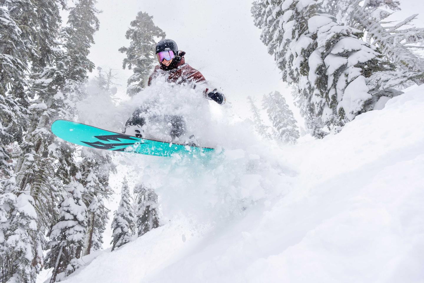 Snowboarder doing a jump in snowy forest.