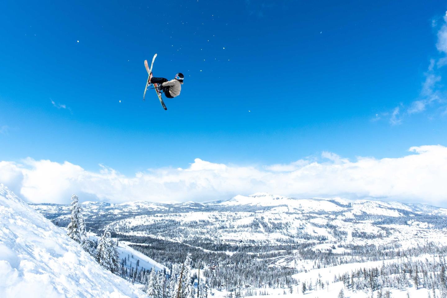 Skier mid-air, blue sky, snowy mountain backdrop.