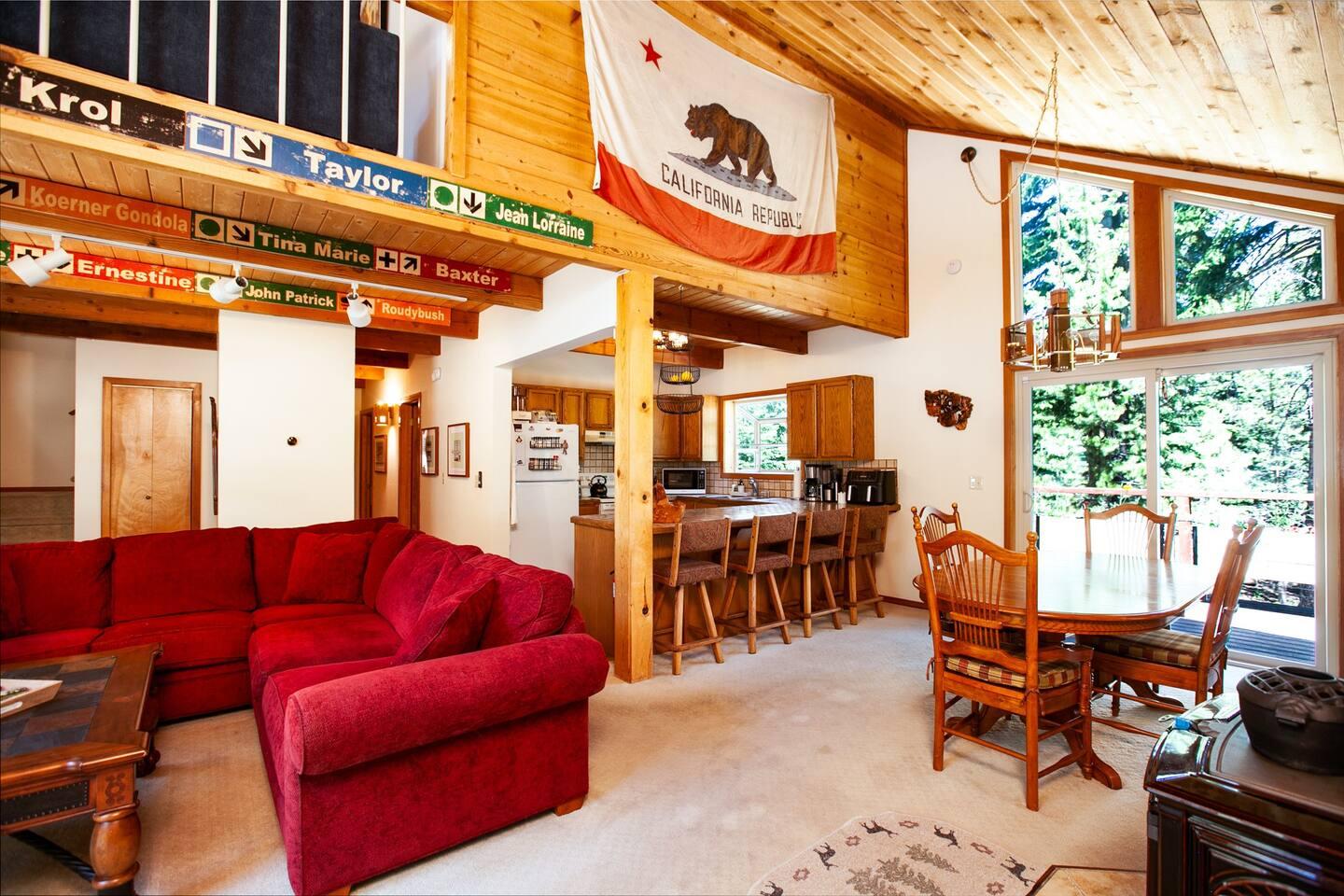 Cozy living room with red sofa, wooden dining set, and large windows.