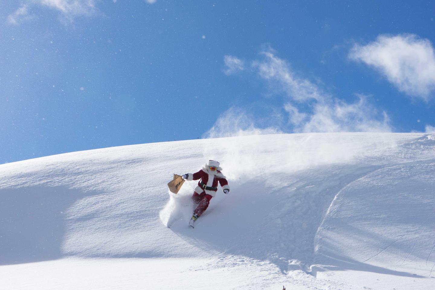 Santa skiing down a snowy slope under a clear blue sky.