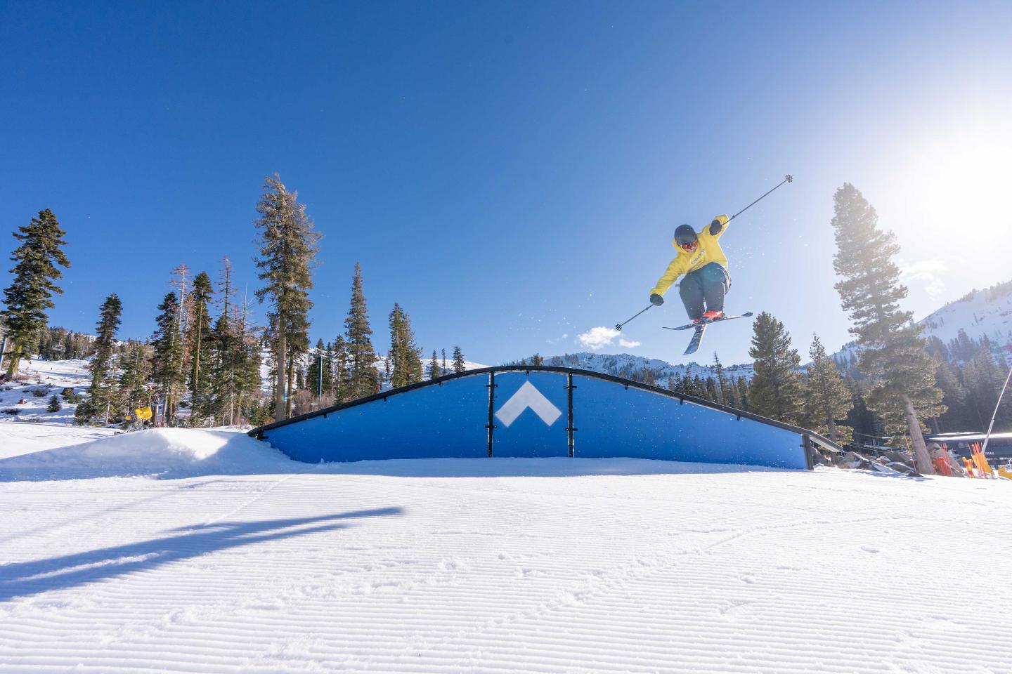 Skier in mid-air jump on snowy slope under clear blue sky.