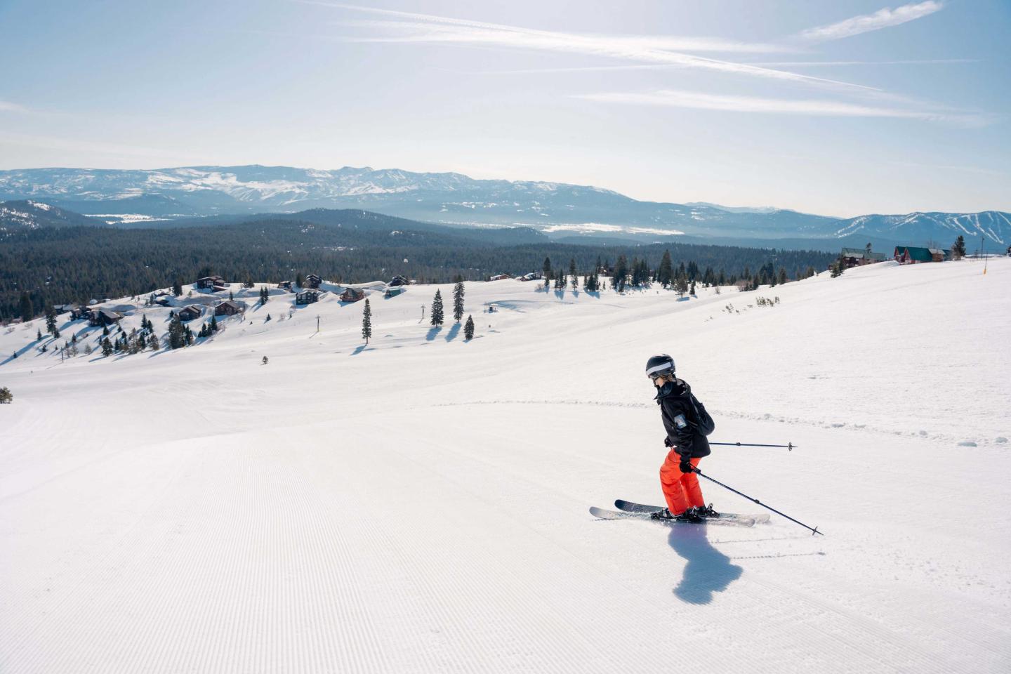 Skier in bright snow gear on a snowy slope with mountains in the background.