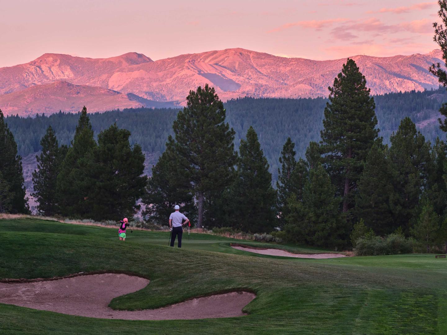 Golf course at sunset, mountains in the background, person with child walking.