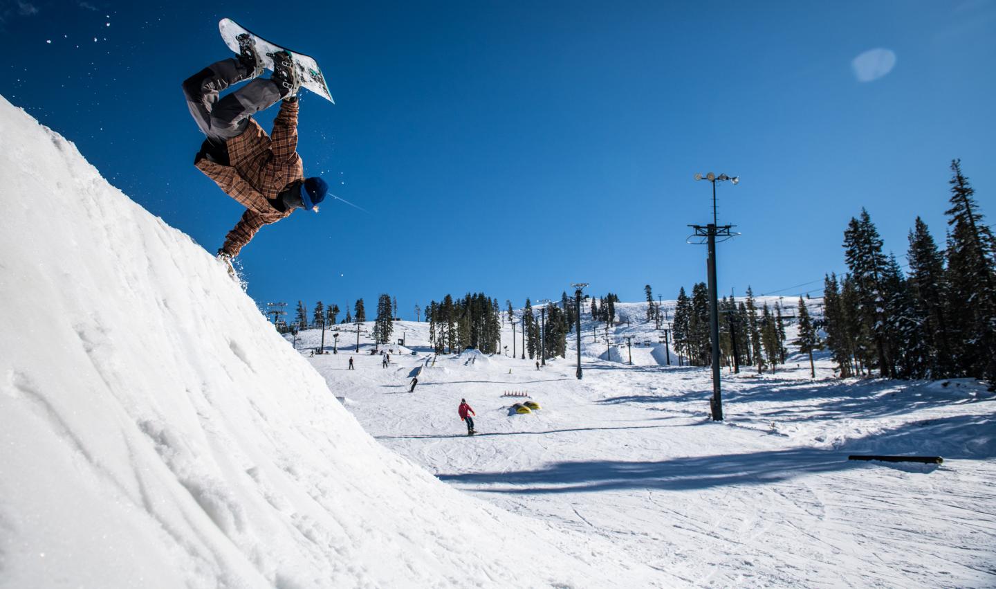 Snowboarder performing a jump on a sunny slope, clear blue sky.