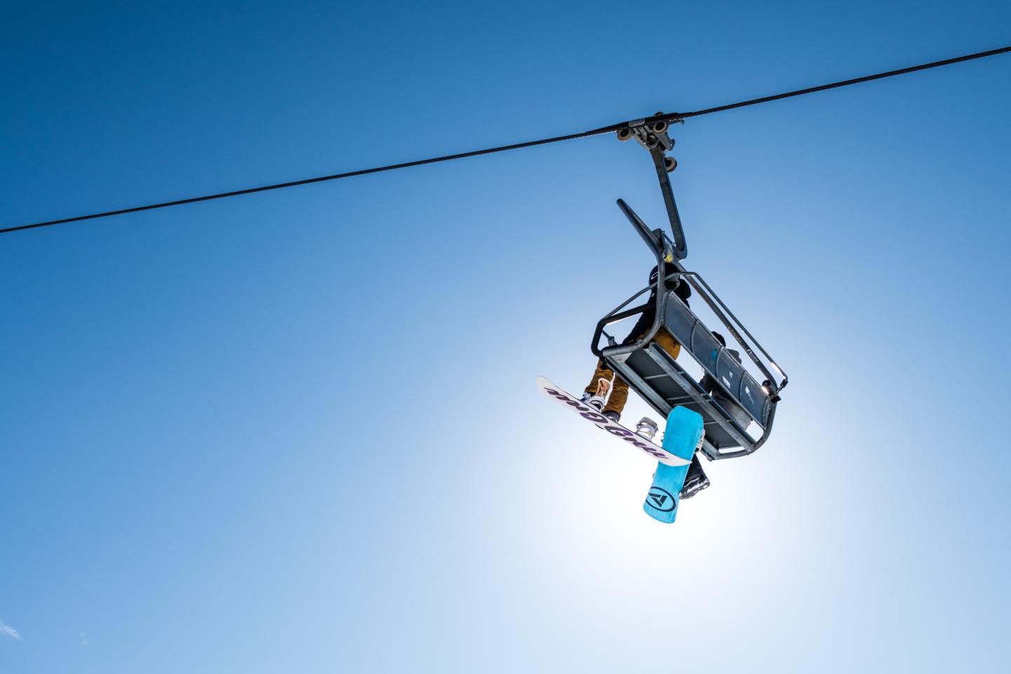 Chairlift with a snowboarder under a clear blue sky.