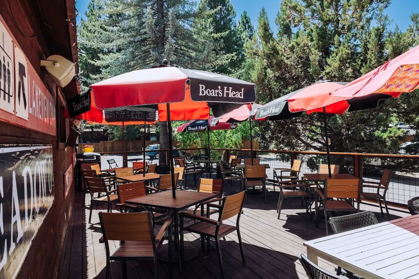 Outdoor cafe with red umbrellas, wooden tables, and chairs on a sunny day.