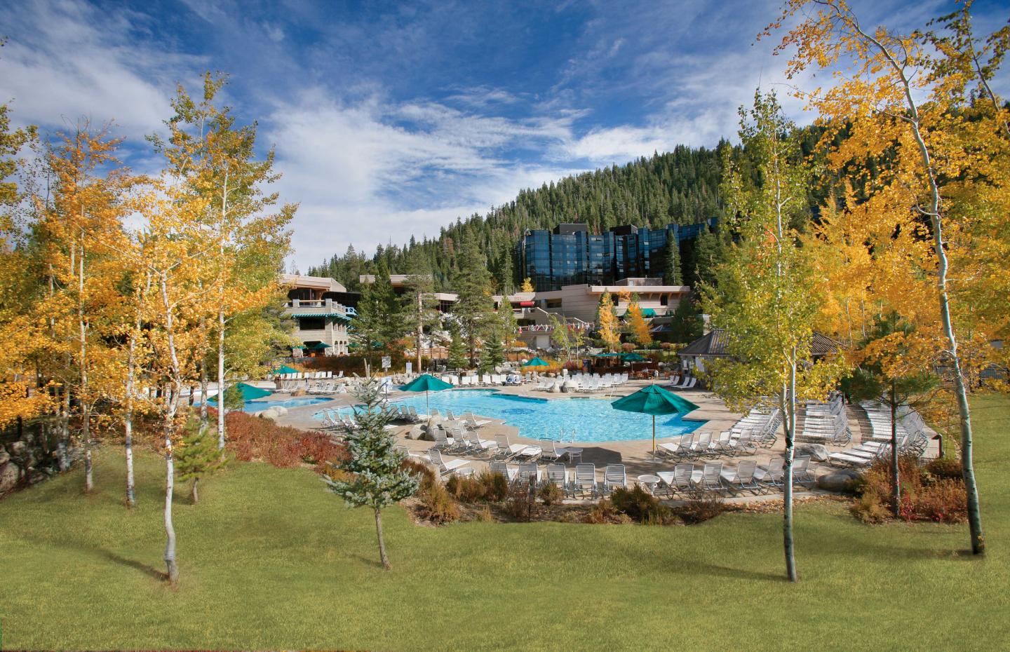 Outdoor pool with lounge chairs surrounded by autumn trees and hills under a blue sky.