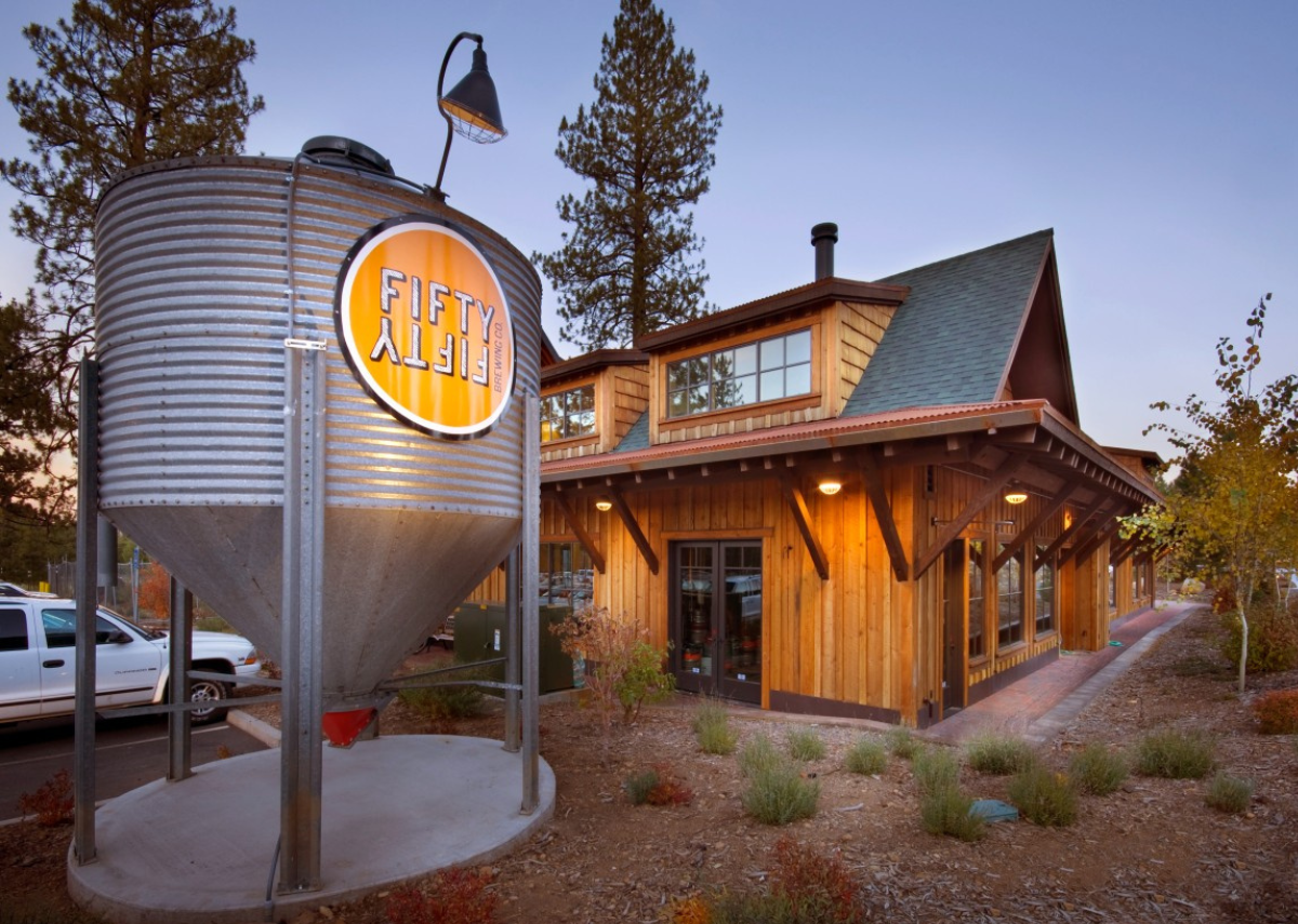 Brewery exterior with silo and wooden building at dusk.