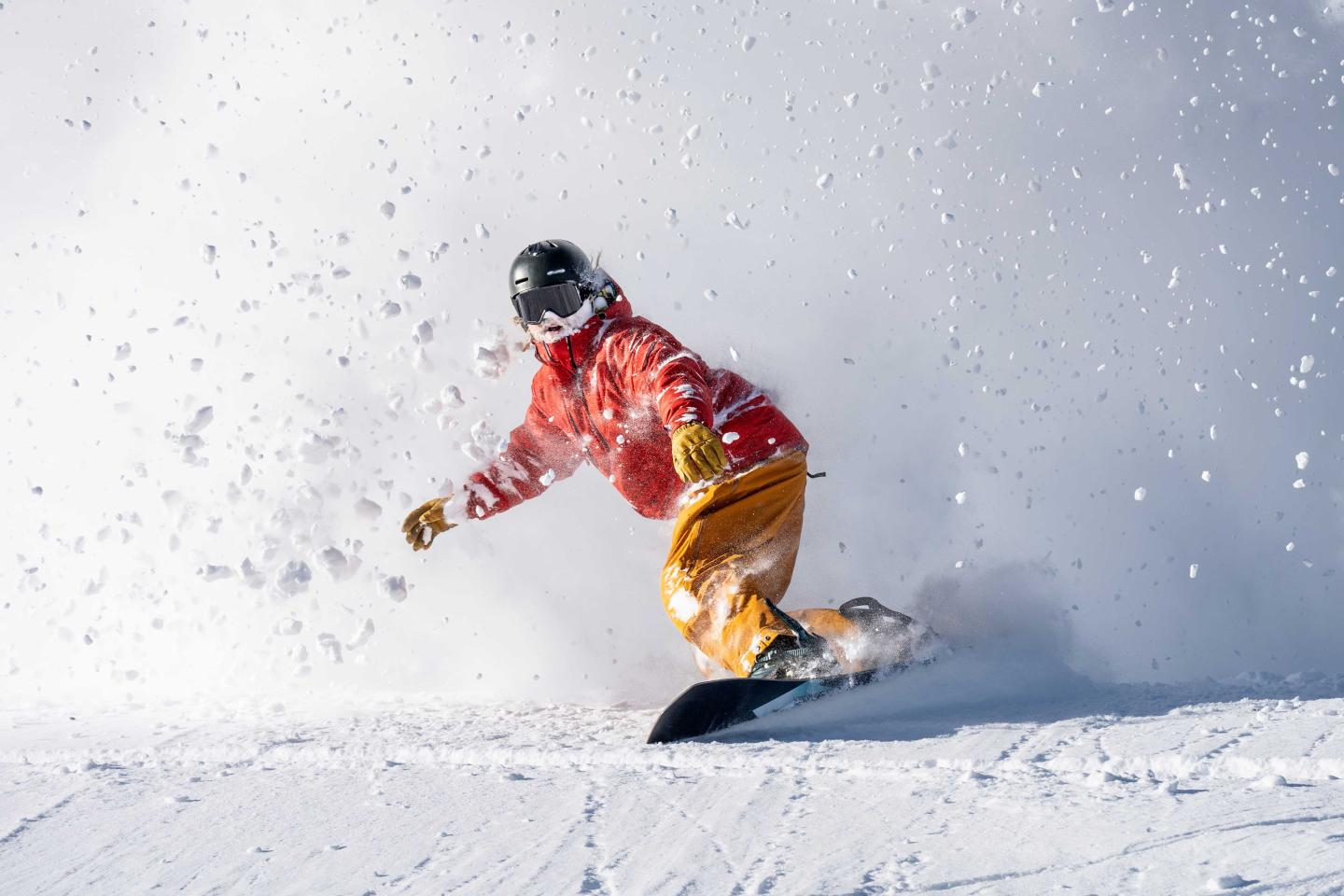 Snowboarder in red jacket and yellow pants on a snowy slope.