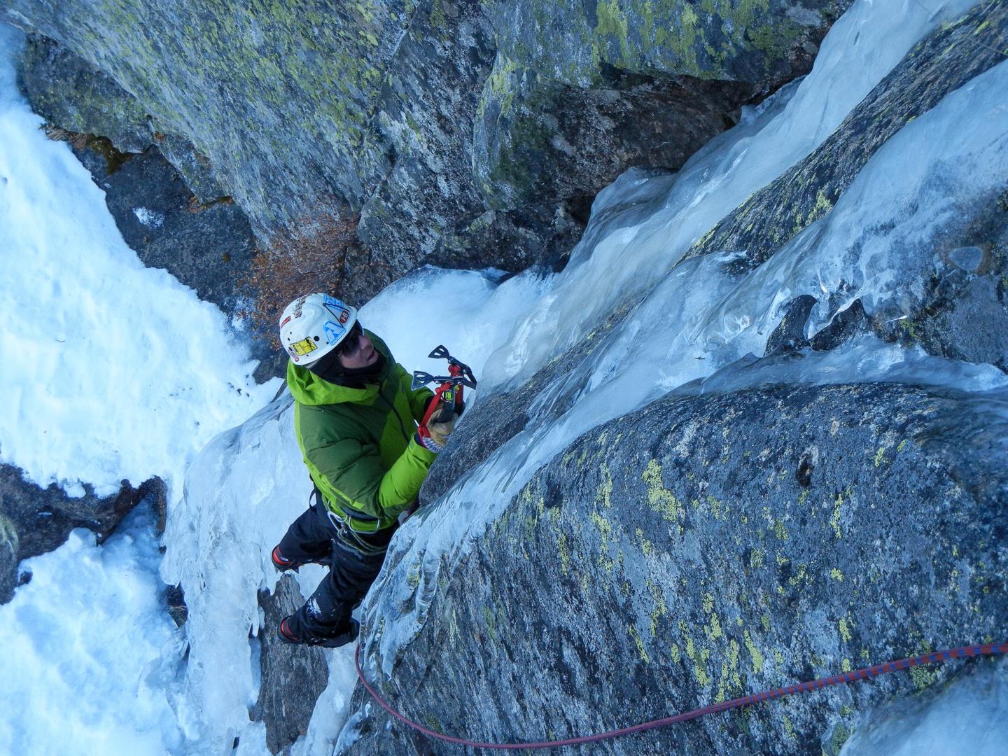 Climber scaling an icy rock face in winter gear.