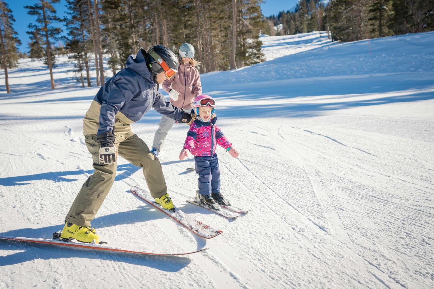Adults teaching a child to ski on a sunny snow-covered slope.