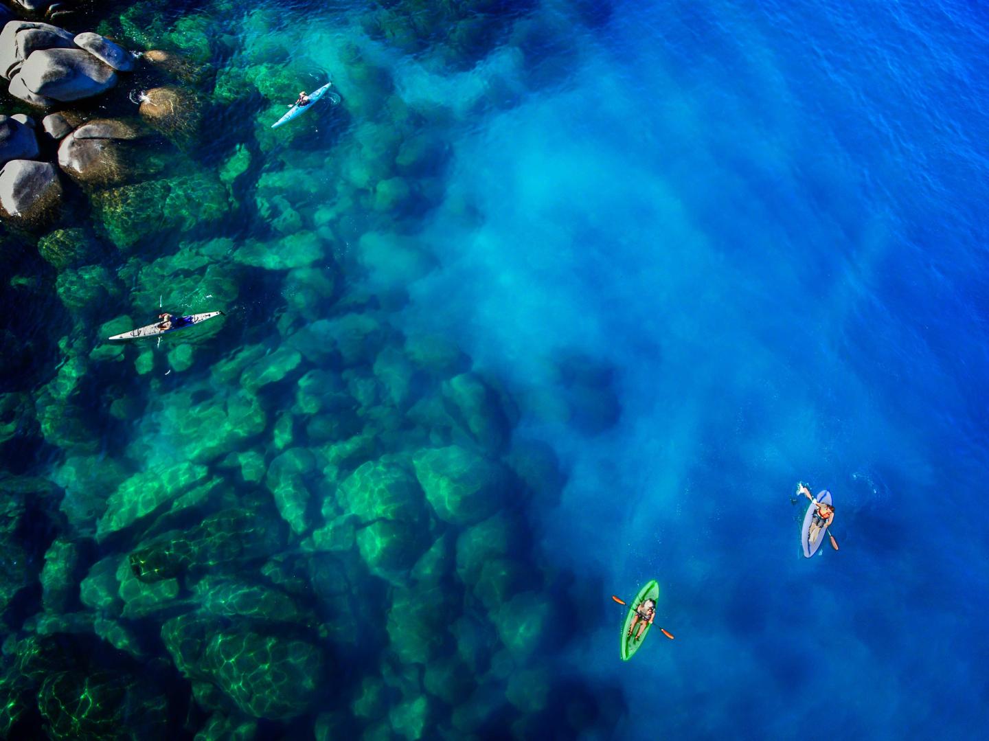 Kayakers in clear blue water near rocky shoreline.