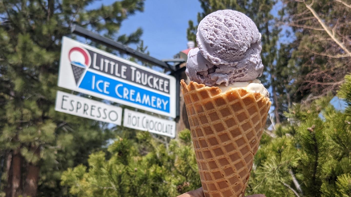 Little Truckee Ice Creamery - Lavender ice cream cone held up with trees and shop sign in the background.
