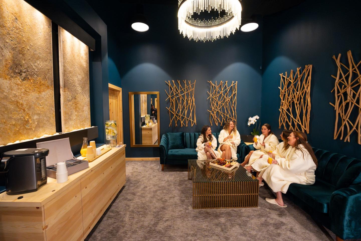 Martis Valley Massage // Elegant spa room with four women in robes lounging on a blue couch, sipping drinks.