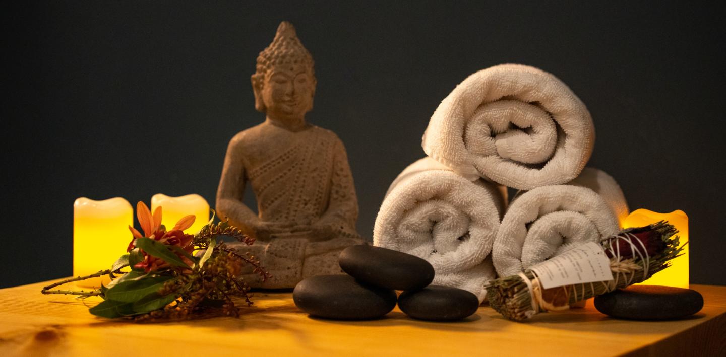 Martis Valley Massasge // Buddha statue, rolled towels, stones, sage, and candles on a wooden surface.