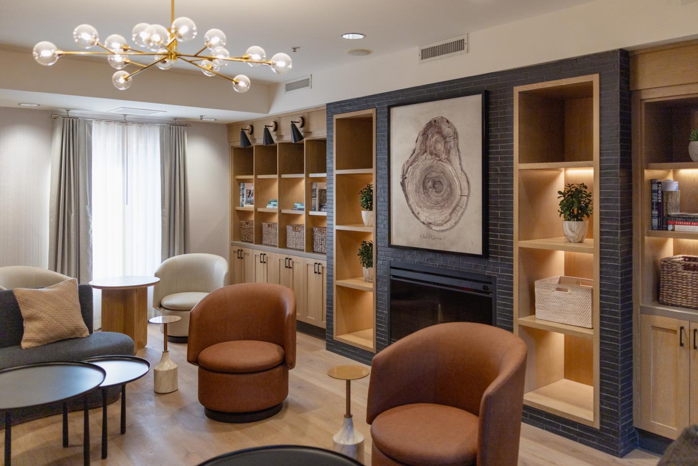 Modern lounge with brown chairs, shelves, and a central chandelier.