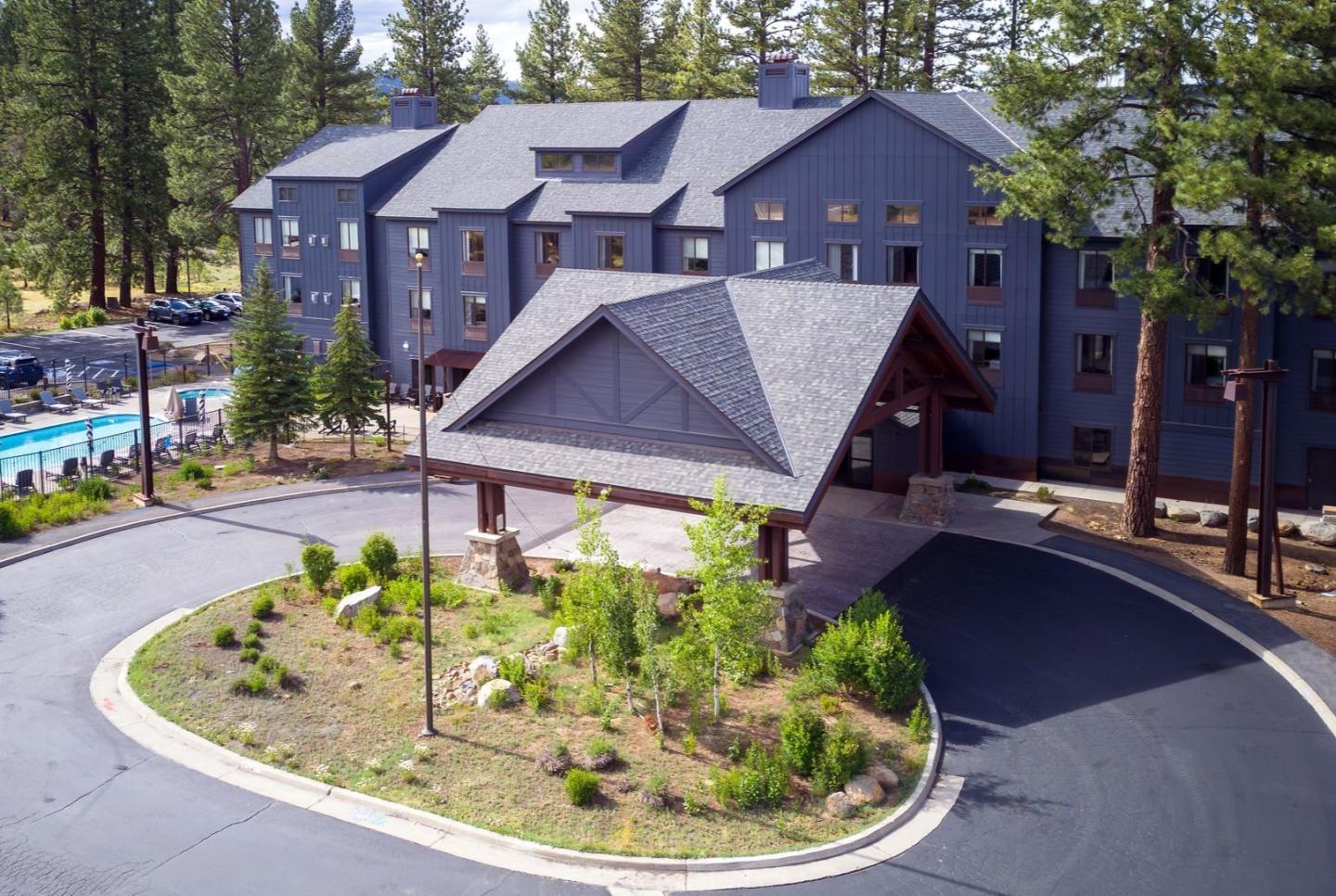 Mountain lodge with a pool, surrounded by pine trees.