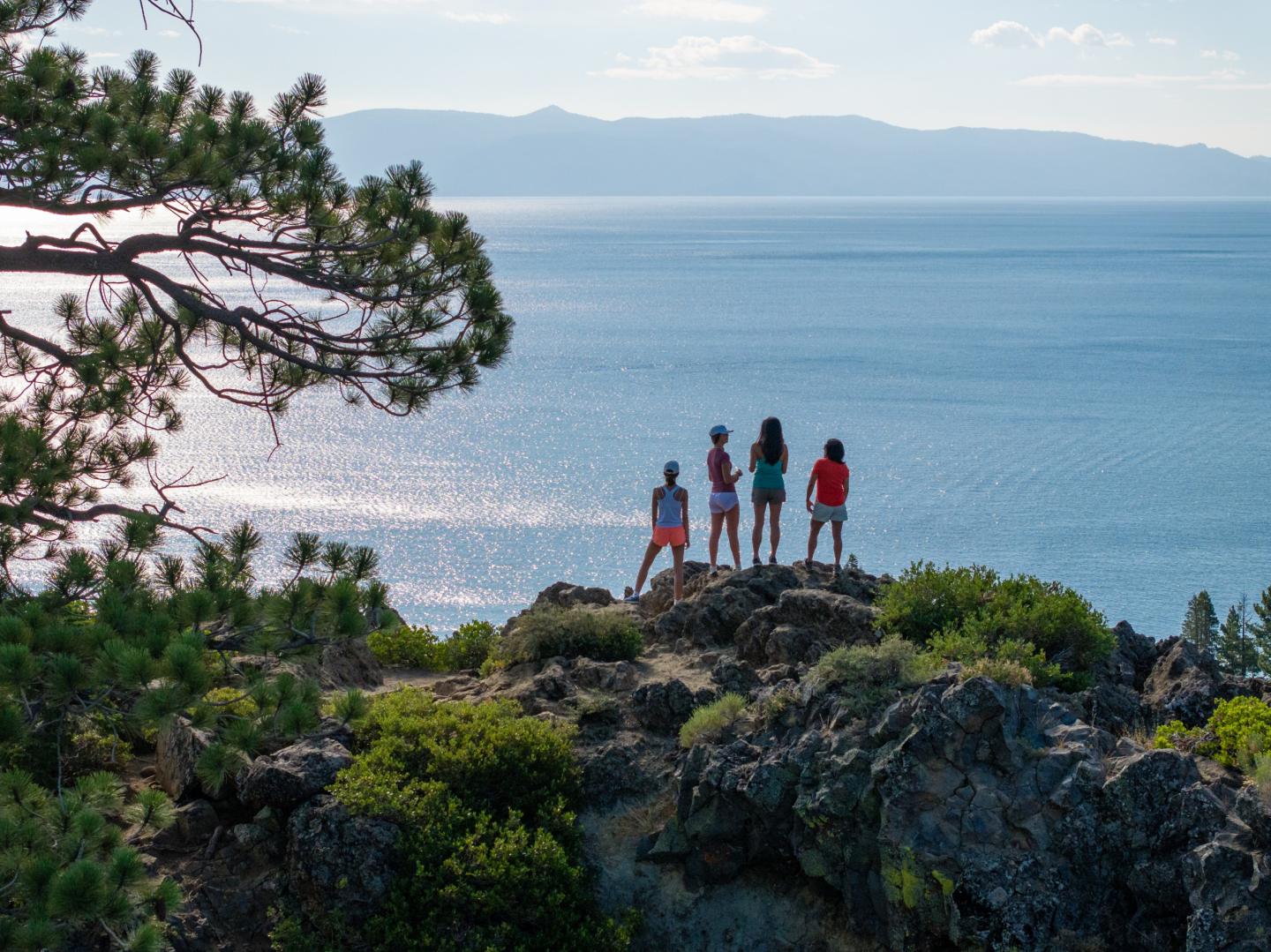 Eagle Rock Four people stand on a rocky cliff, overlooking a vast blue lake under a clear sky