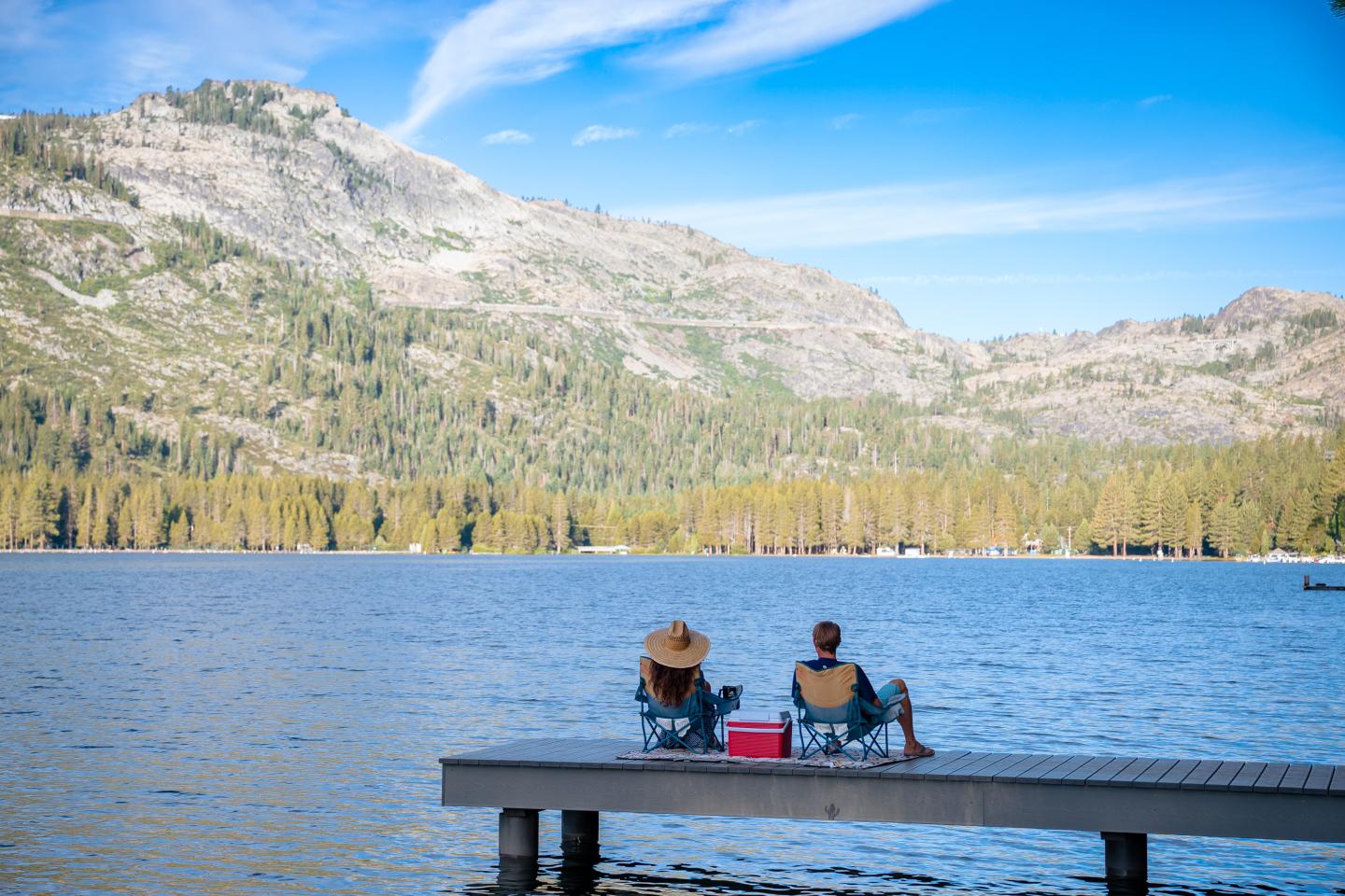 Two people relax on a lakeside Donner dock with mountain views.