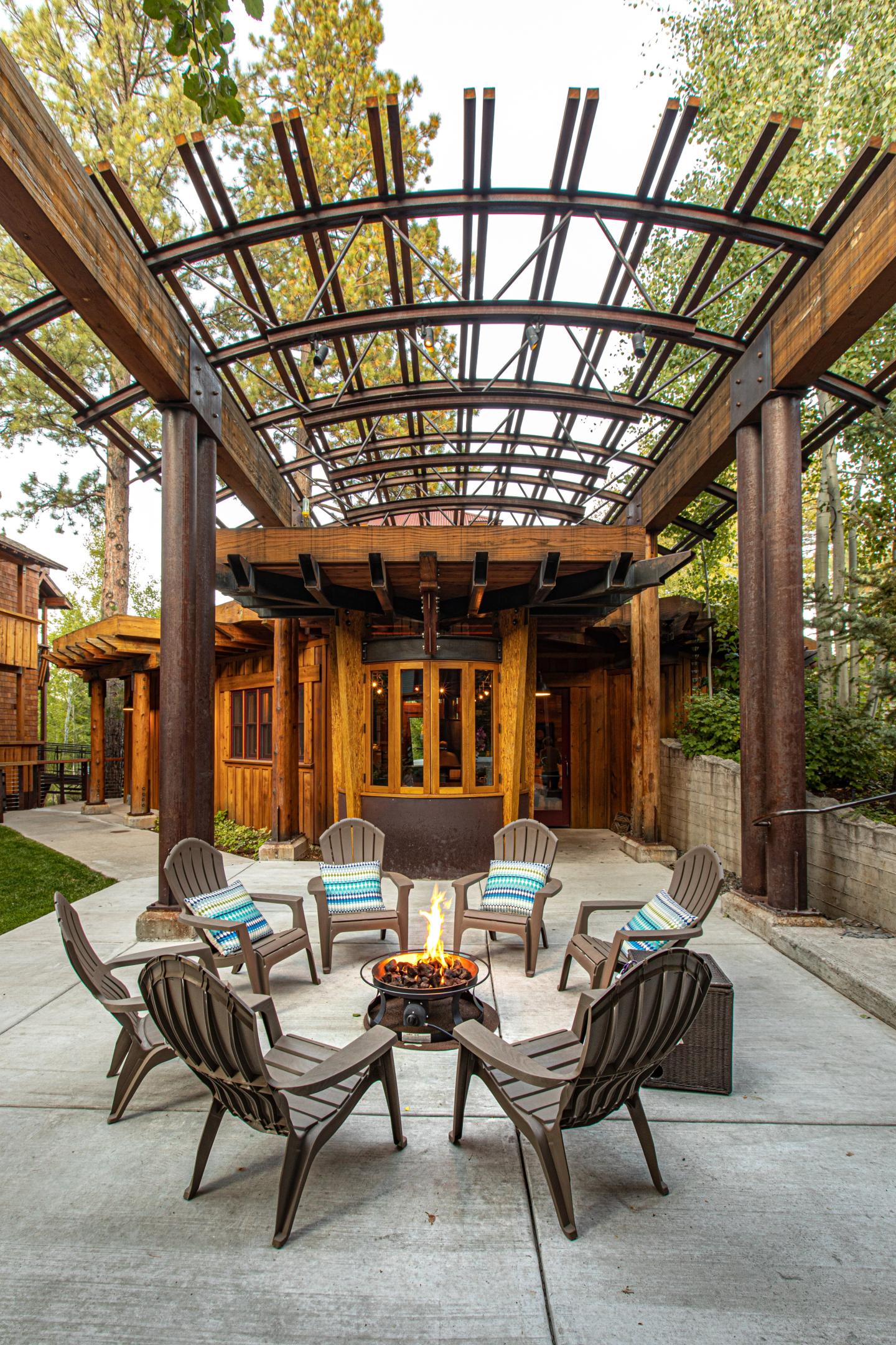 Patio with wooden chairs around a fire pit, under an arched pergola.