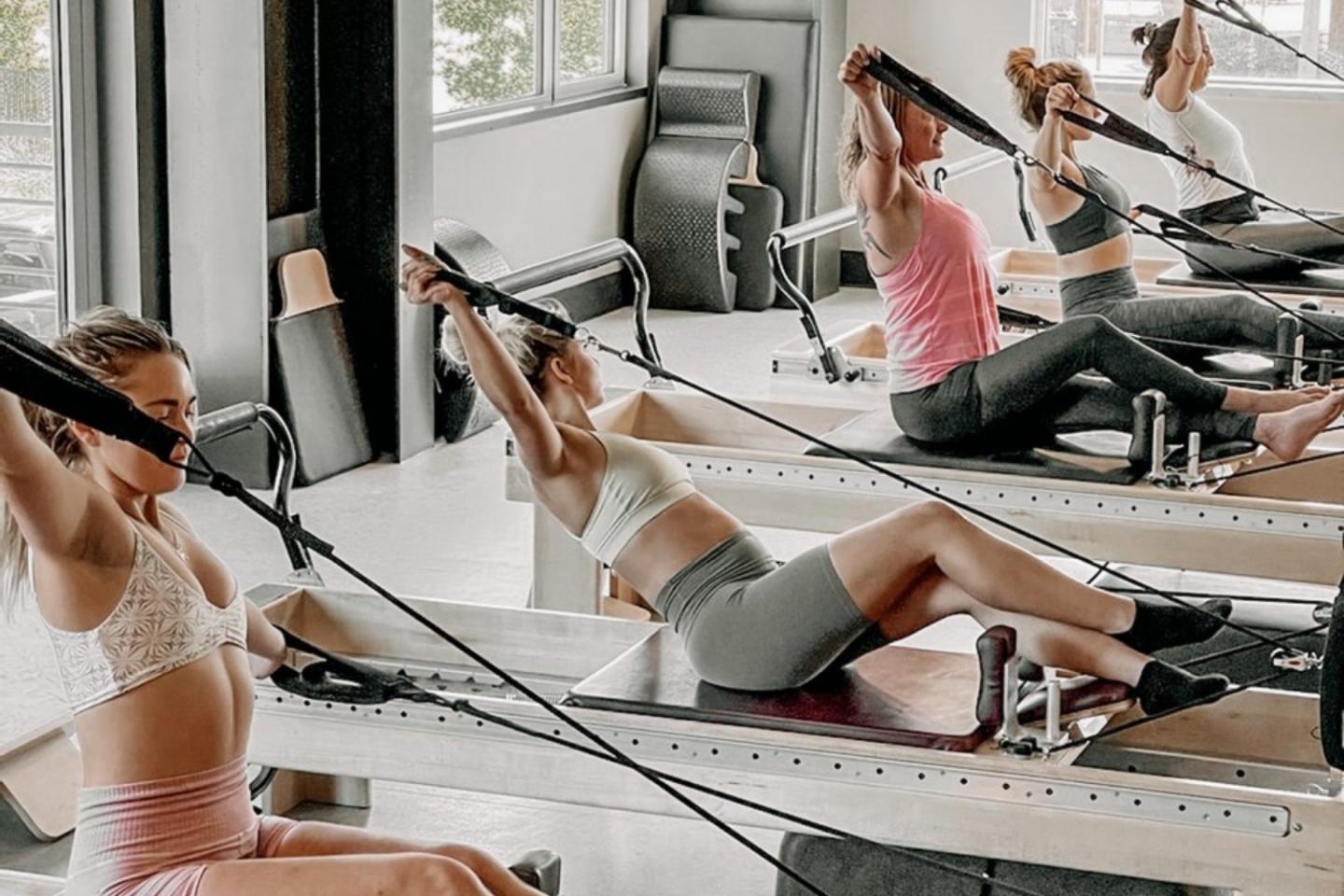 Women exercising on Pilates reformers in a bright studio.