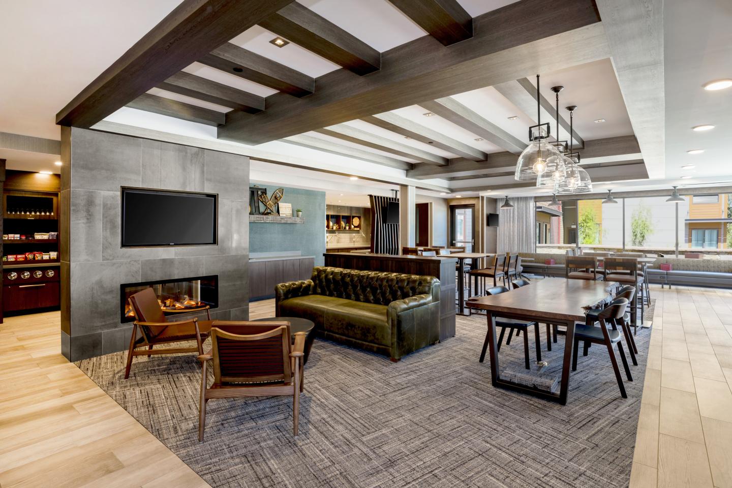 Modern lounge with green sofa, wooden chairs, dining table, and a wall-mounted TV. SpringHill Suites Marriott in Truckee California