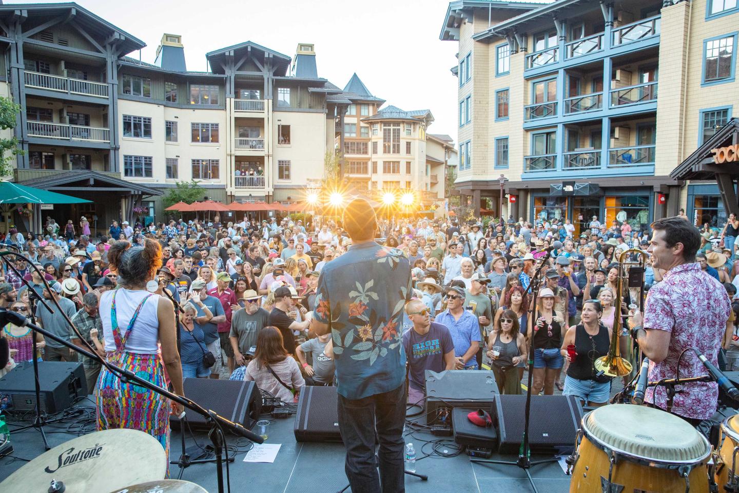 Band performing to a large outdoor crowd in a plaza at sunset.