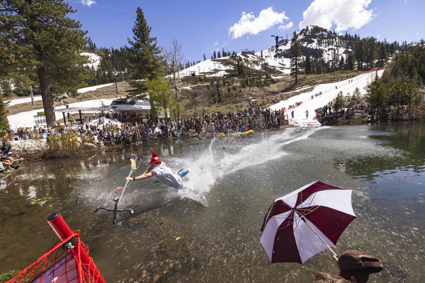 Skier splashing into a pond, surrounded by spectators on a snowy mountain slope. Cushing Crossing at Palisades Tahoe