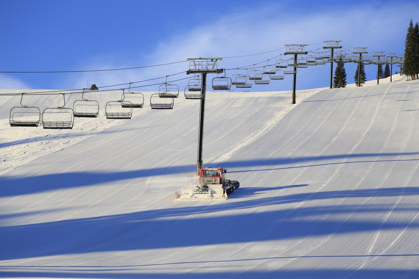 Snow-covered ski slope with chairlift and snow groomer.