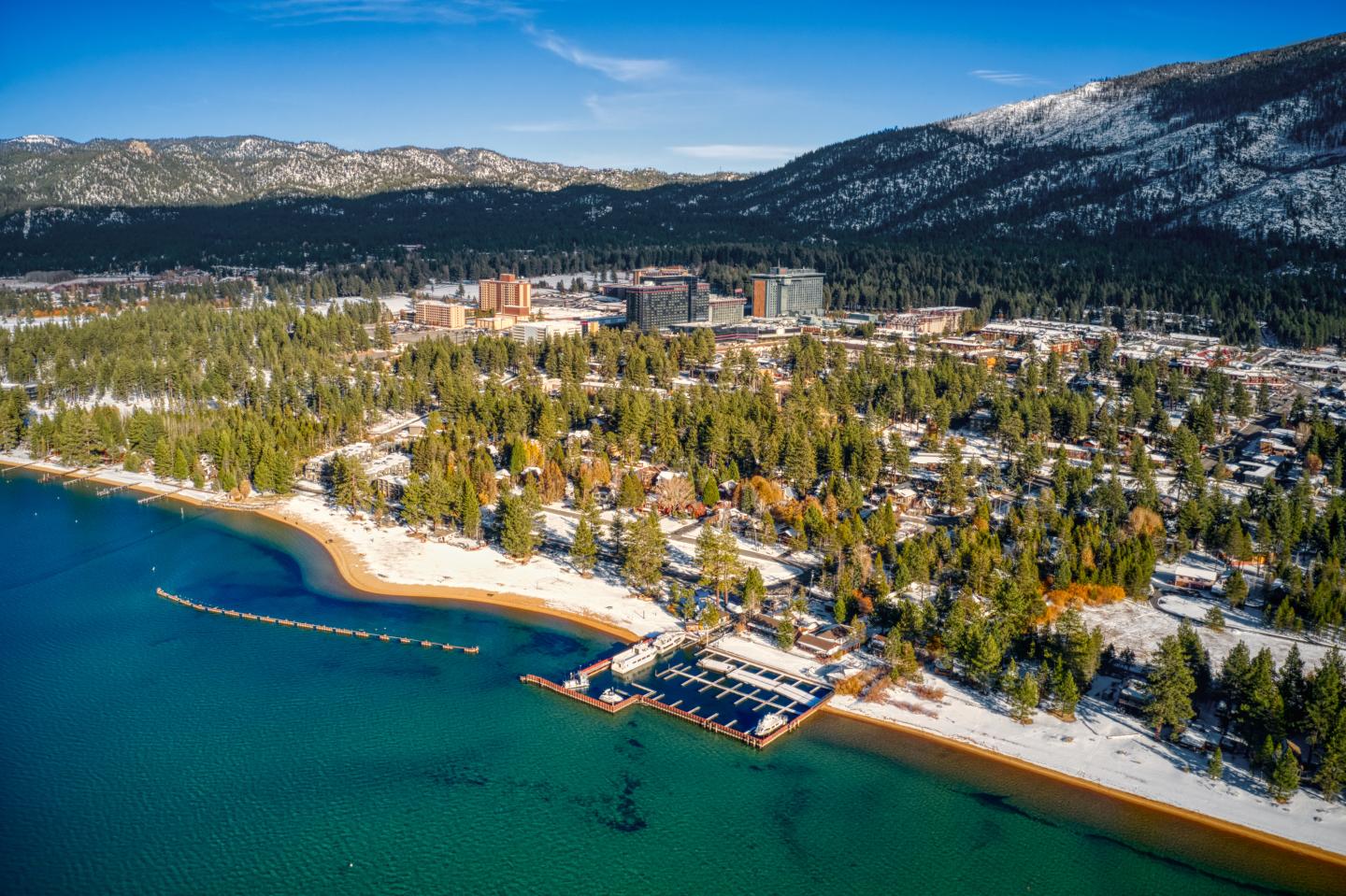Aerial view of a snowy South Lake Tahoe town with mountains in the background.