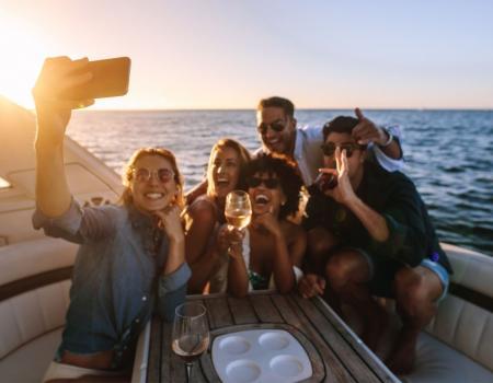 Tahoe Getaways Fall Lodging Deal / Friends taking a selfie on a boat at sunset, smiling and holding drinks.