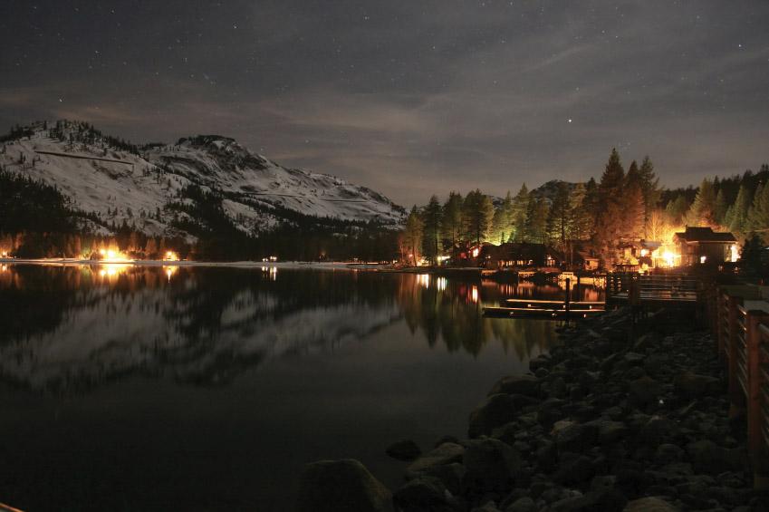 Donner Lake Village / Mountain lake at night, lights reflecting on calm water, snowy peaks, and trees.