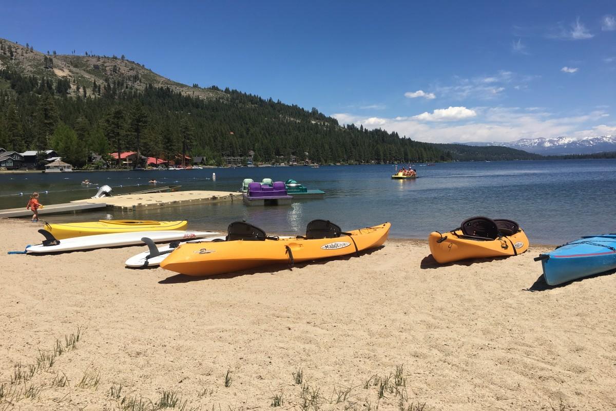 West End Beach // Kayaks on a sandy beach by a lake, mountains in the background.