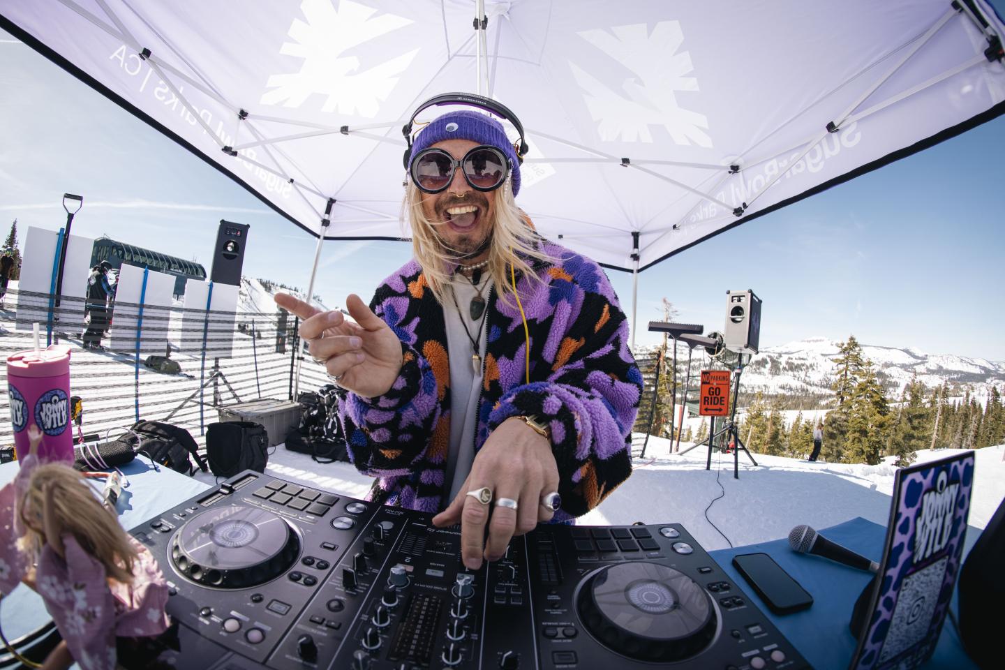 DJ performing at an outdoor snowy venue under a canopy.
