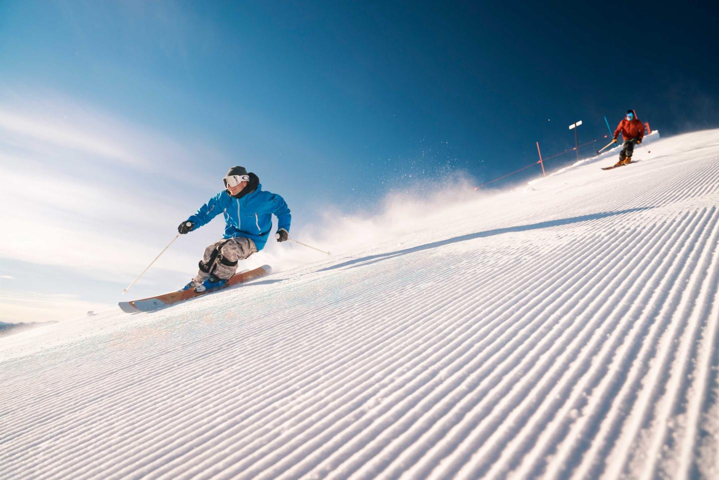 Two people skiing on a sunny, groomed slope.