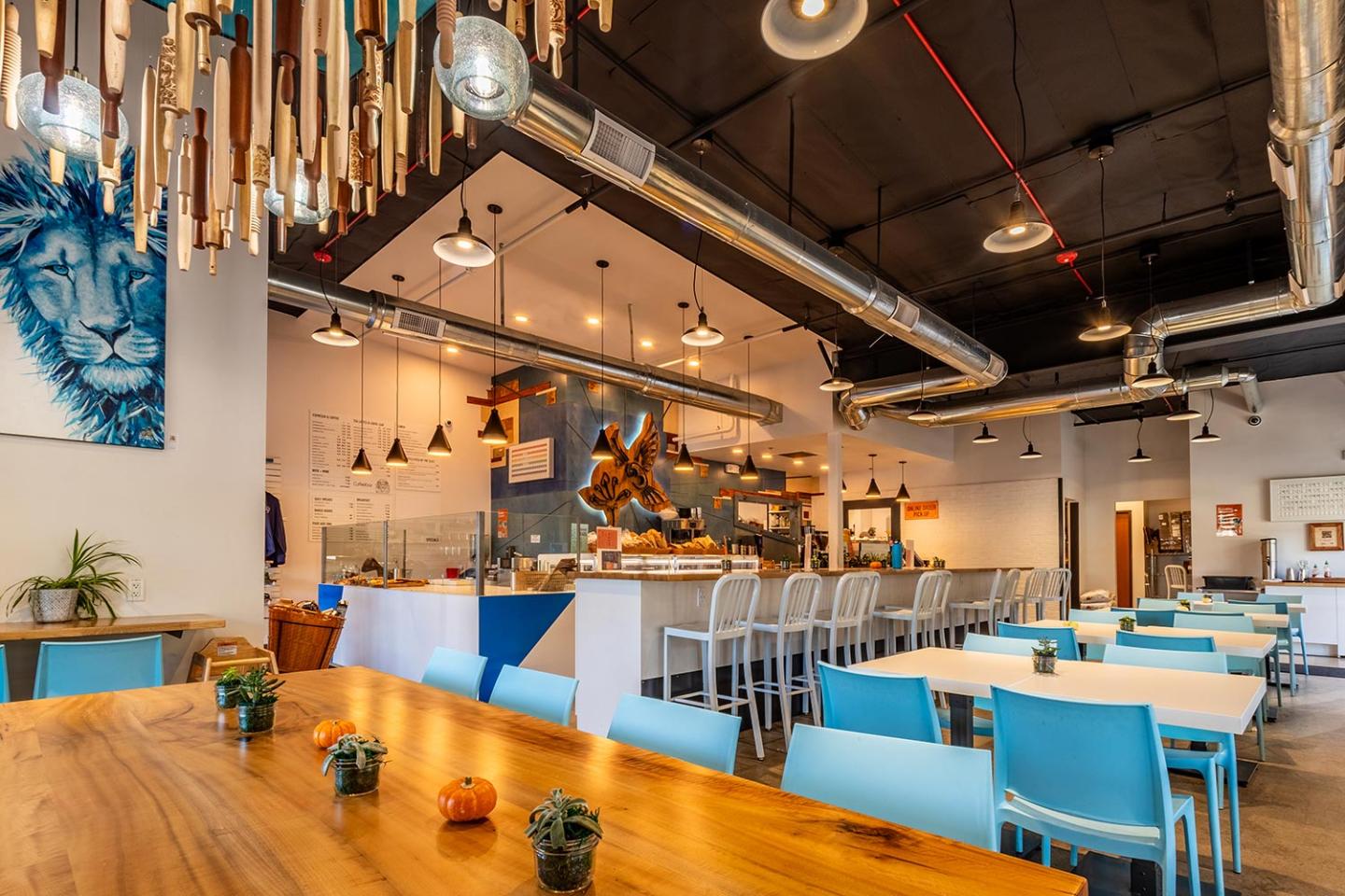 Modern cafe with blue chairs, wooden tables, and decorative ceiling lights.