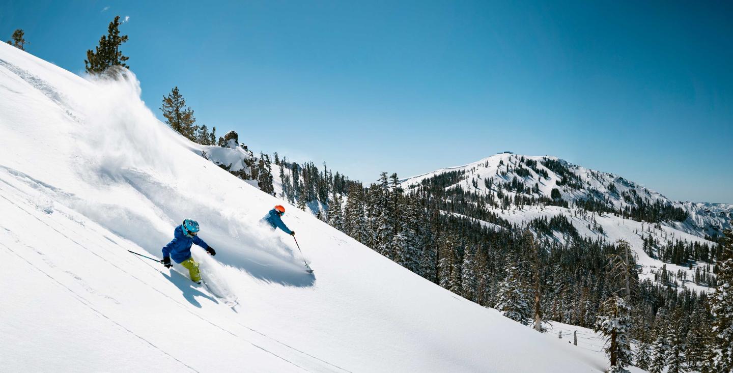 Skiers racing down a snowy mountain under a clear blue sky.